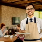 Male waiter in an apron serving food in a Dubai hotel restaurant setting